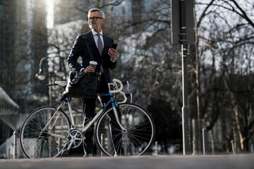 Grey-haired businessman with bicycle and coffee to go in the city