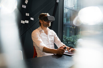 Business man with virtual reality glasses and tablet sitting in modern office
