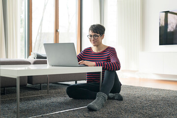 Portrait of woman sitting on the floor of living room using laptop