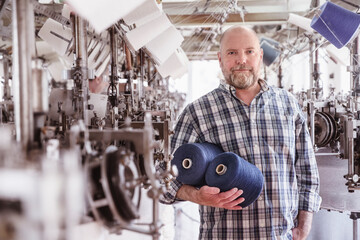 Portrait of man holding cotton reels in a textile factory