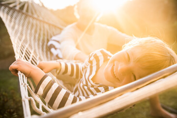 Portrait of smiling boy lying in hammock with father in background