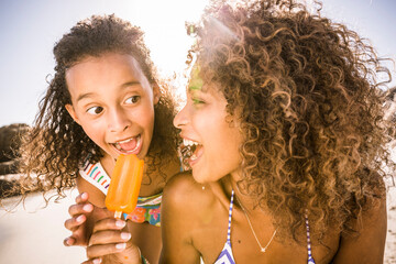 Woman sharing popsicle with daughter on the beach