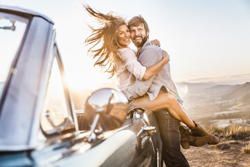 Happy couple at convertible car in the countryside at sunset