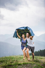Happy couple running on a meadow in the mountains in rain, Achenkirch, Austria