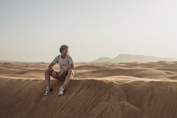 Male tourist looking away while sitting on sand dunes in desert at Dubai, United Arab Emirates