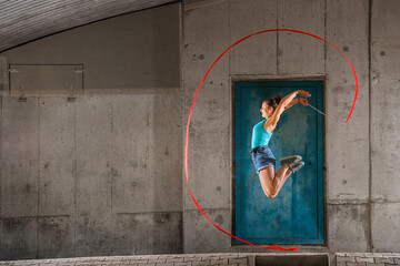 Young woman holding ribbon jumping while doing aerobics against concrete wall
