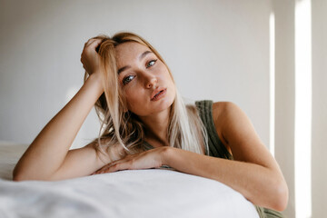 Fototapeta premium Seductive young woman with hand in hair leaning bed at home