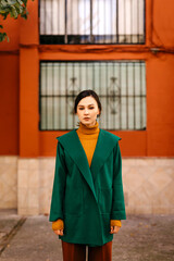 Young woman wearing green jacket standing against building in city