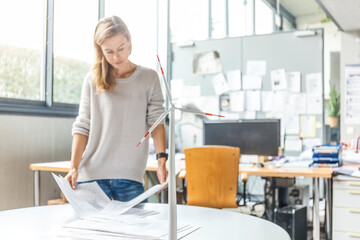 Woman in office working on plan with wind turbine model on table