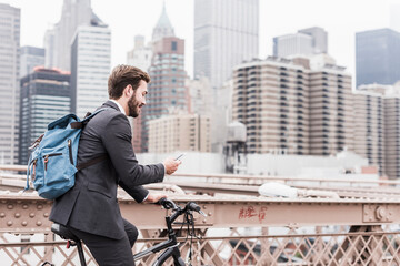 USA, New York City, businessman on bicycle on Brooklyn Bridge using cell phone