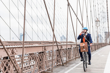 USA, New York City, man on bicycle on Brooklyn Bridge using cell phone