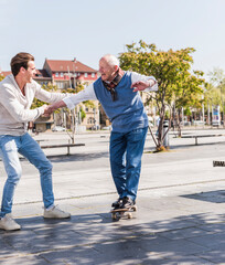 Adult grandson assisting senior man on skateboard