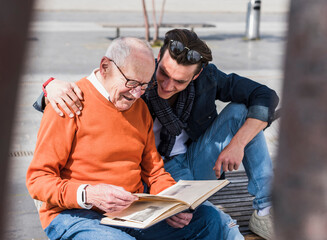 Senior man and adult grandson on a bench looking at photo album