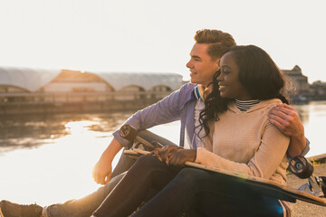 Young couple sitting at the river, watching sunset