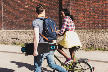 Young couple with bicycle and skateboard walking in the street - obrazy, fototapety, plakaty