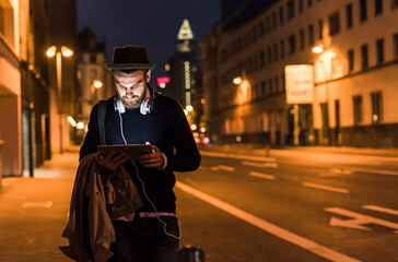 Stylish young man with tablet on urban street at night
