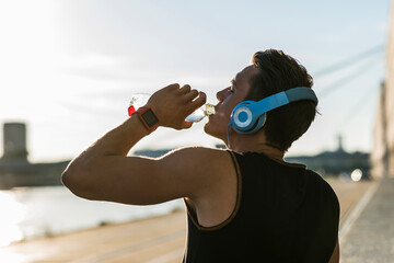 Young man wearing headphones, drinking water