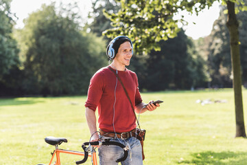 Laughing man with racing cycle listening music with headphones in a park