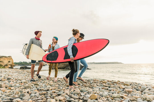 Happy friends with surfboards walking on stony beach