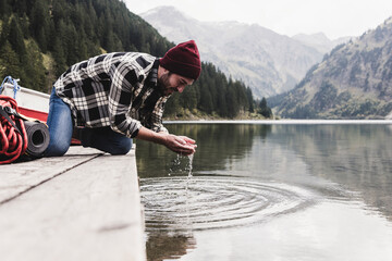 Austria, Tyrol, Alps, man kneeling on jetty scooping water from mountain lake