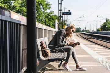 Young woman sitting at train station, using digital tablet