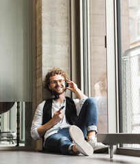 Happy casual young man listening to music with headphones at the window