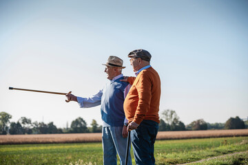Two old friends standing in the fields, pointing with walking stick