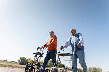 Two old friends walking on a country road, using wheeled walkers