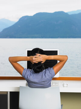 Woman Using Computer in Front of Window with Ocean View