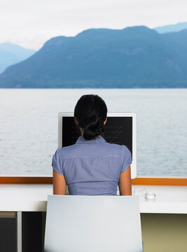 Woman Using Computer in Front of Window with Ocean View