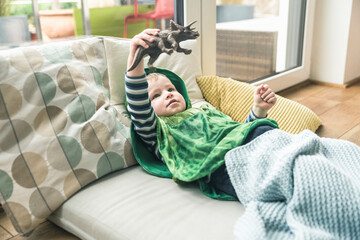 Boy in a costume lying on amattress playing with toy figure at home