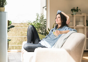 Smiling woman with a glass of infused water sitting on the couch at home