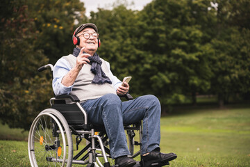 Portrait of happy senior man sitting in wheelchair listening music with smartphone and headphones