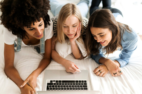 Three girlfriends lying on bed sharing laptop