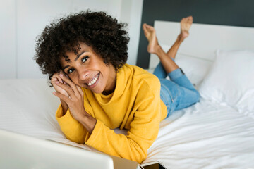 Portrait of happy woman lying on bed with laptop