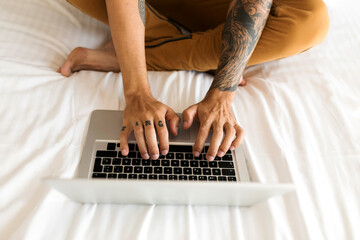 Close-up of tattooed man using laptop in bed