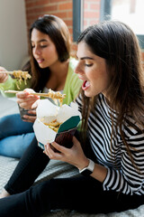 Two young women having Asian takeaway food at home
