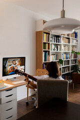 Back view of boy sitting on arm chair at home using online tutorial for learning to play guitar