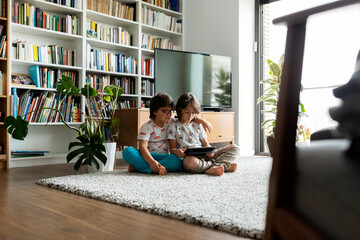 Two brothers sitting on floor in the living room with digital tablet