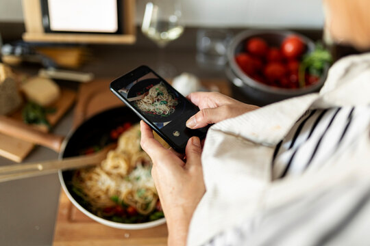 Close-up of woman taking smartphone picture of her pasta dish in kitchen at home