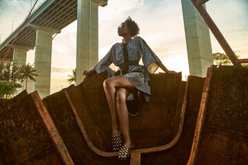 Woman wearing dress and sitting on rusty ship wreck