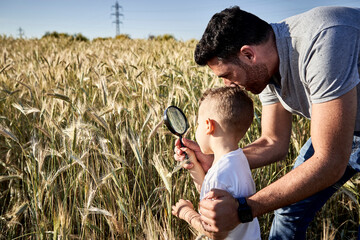 Father and son examining crops with magnifying glass in agricultural field