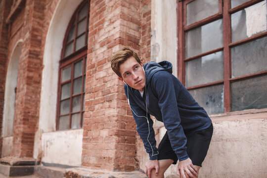 Young man with earphones at brick building looking around