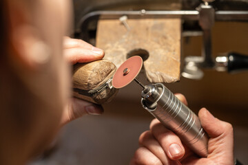 Hand of female goldsmith working with grinder on silver ring