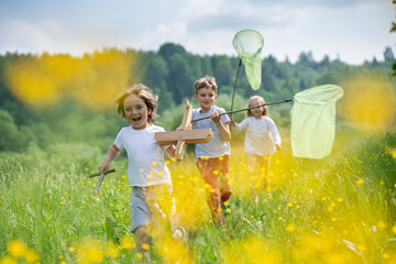 Carefree friends with model airplane and butterfly nets running on grassy land in forest