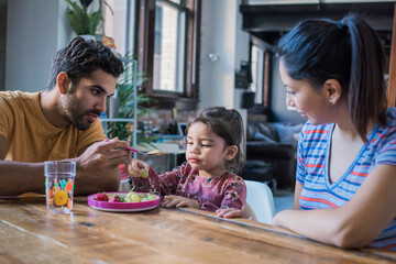 Mother and father feeding their little daughter in kitchen