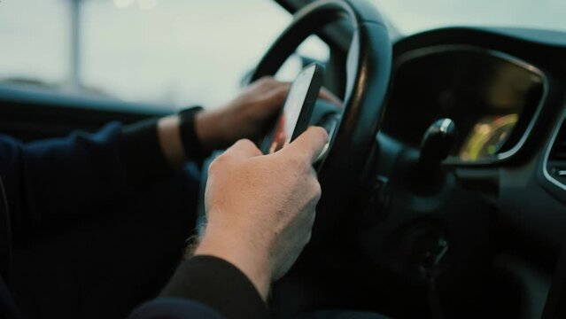 Unrecognizable man driver sitting at steering wheel and browsing smartphone