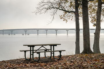 Fototapeta na wymiar picnic table at Colbert Ferry Park, Natchez Trace Parkway with a view of the bridge over Tennessee River from Tennessee to Alabama, foggy November morning