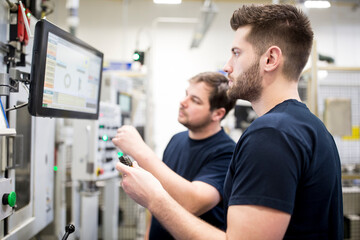 Two men working in a modern factory operating a machine together