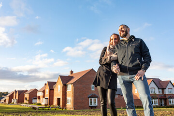 Happy couple looking away while standing outside newly built houses against sky - obrazy, fototapety, plakaty